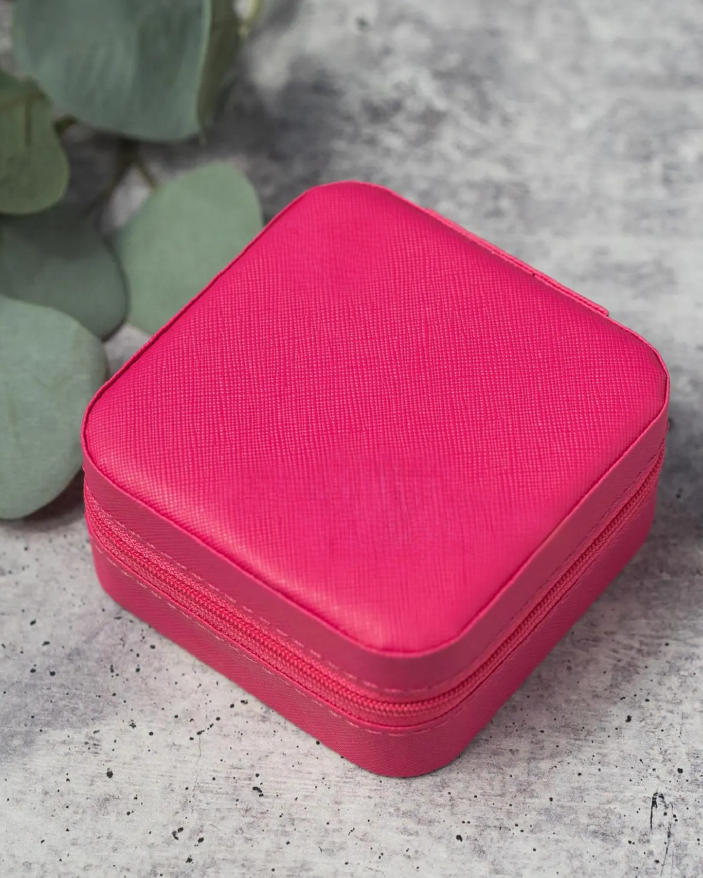 Pink jewelry case on a gray surface with green leaves in the background