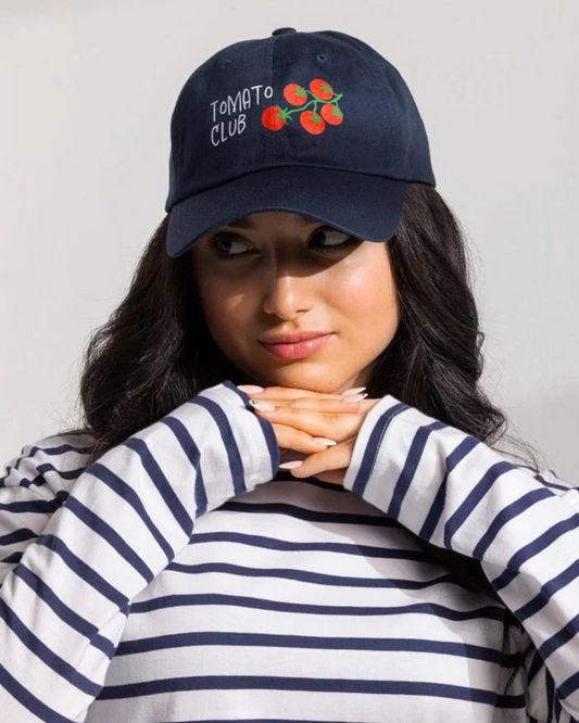 Person wearing a navy blue cap with 'Tomato Club' embroidery against a plain background